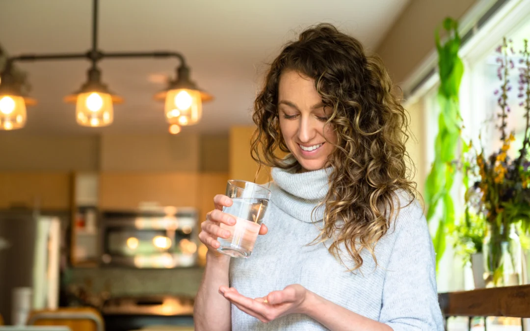 A young woman holds a glass of water as she prepares to take a multivitamin as part of her daily wellness supplement routine.