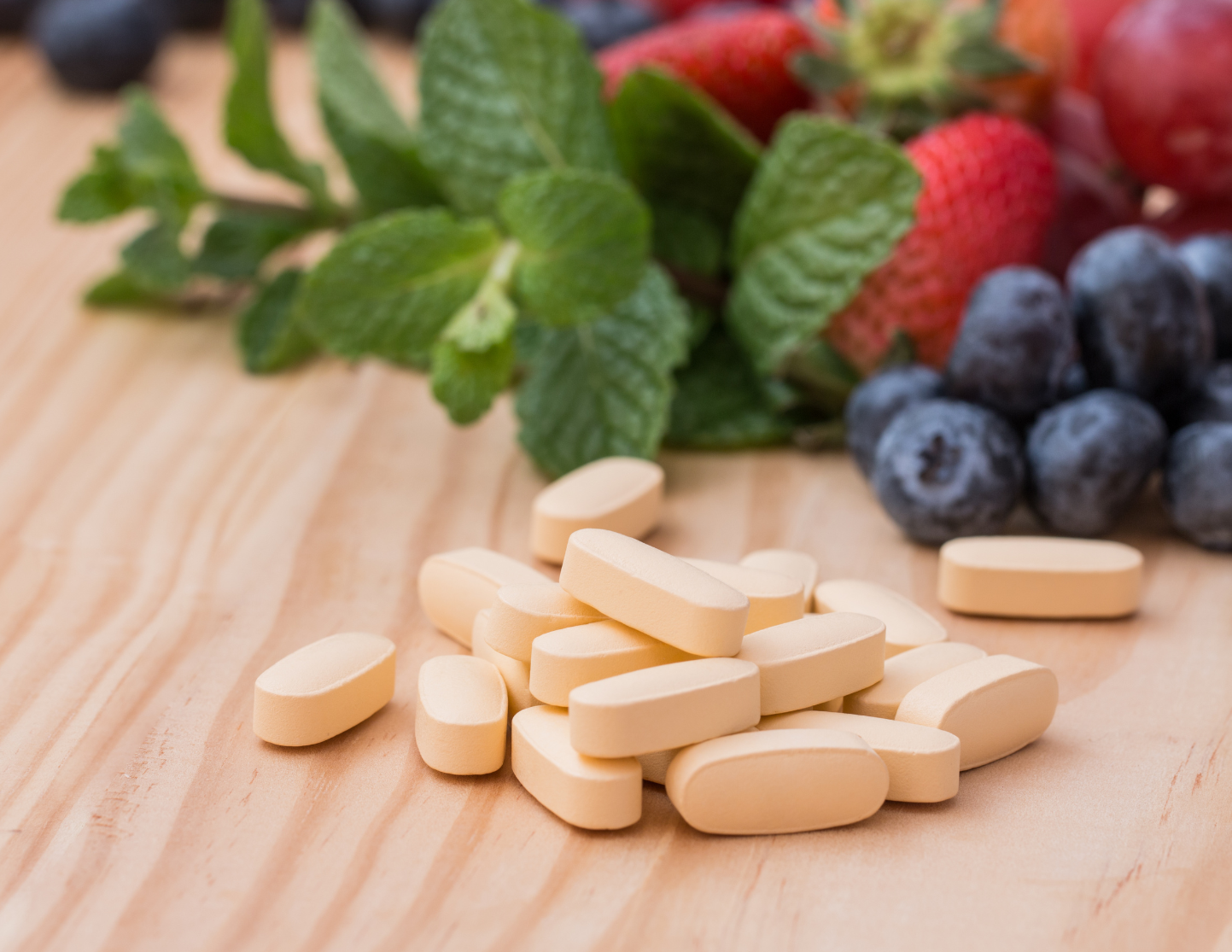 a table top with blueberries, strawberries, mint leaves, and multivitamin tablets