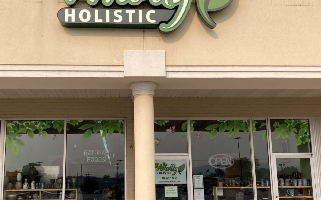 beige building with an unlit wholly holistic logo. large windows filled with pottery make up a storefront.