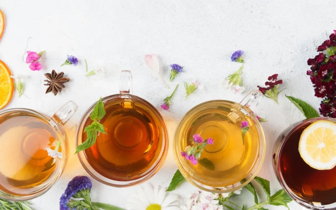 Four colorful herbal mocktail drinks surrounded by scattered flower buds, herbs, and spices, perfect for a refreshing Dry January.